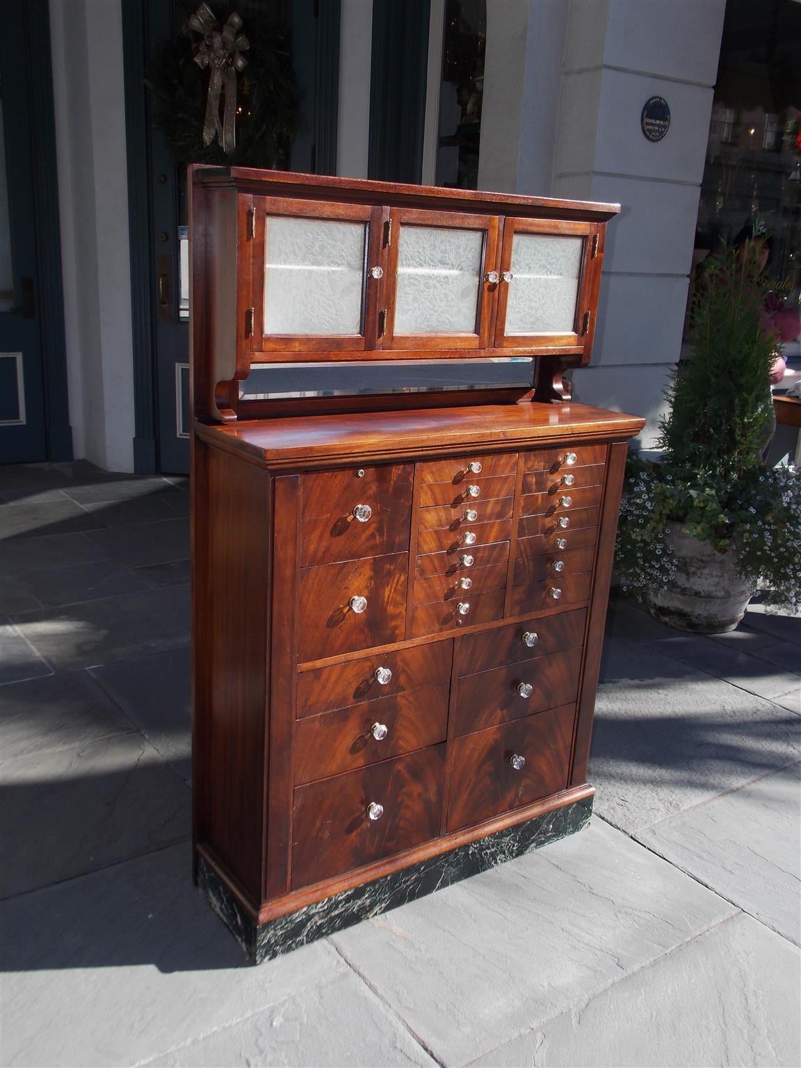 American mahogany compartmentalized twenty-two drawer dental cabinet with upper etched milk glass doors, original crystal and brass knobs, and terminating on rectangular marble plinth.  Late 19th Century