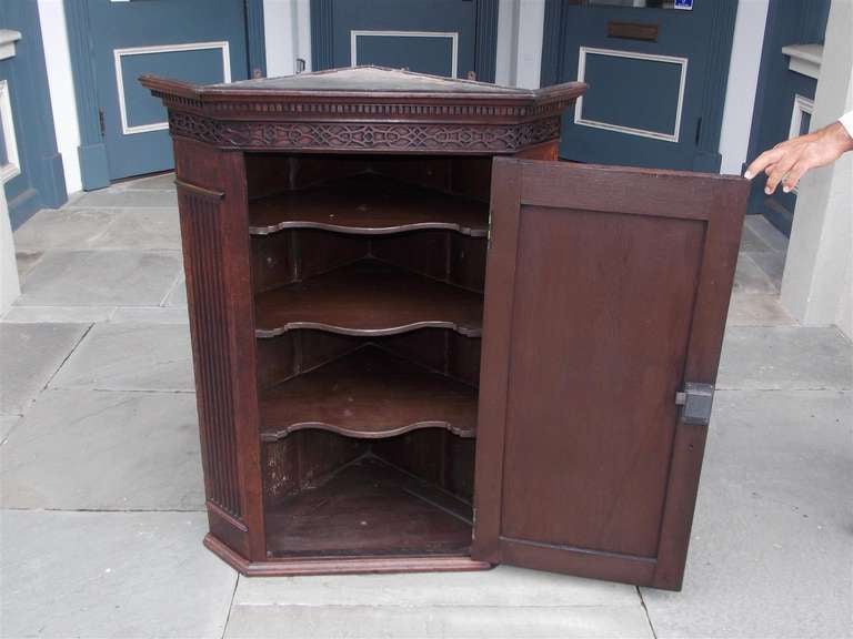 English Oak one door hanging corner cabinet with carved dental molding, articulated fret work, fluted sides, and interior butterfly shelving.  Late 18th Century.