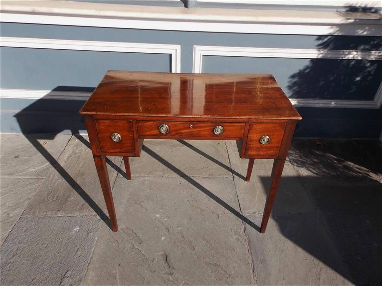 English Hepplewhite mahogany three drawer writing table with circular brasses and terminating on squared tapered legs.  Late 18th Century