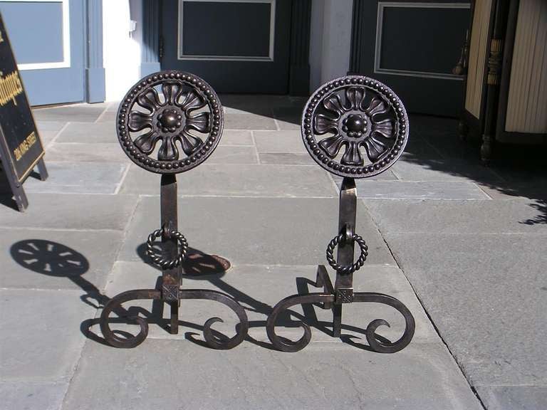 Pair of wrought iron floral medallion andirons with decorative rope rings on squared plinths, and terminating on scrolled legs.  20th Century