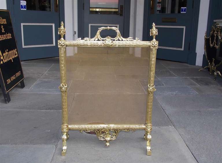 French brass free standing fire screen with centered floral handle, swag finial motif, foliage motif, and terminating on scrolled block feet. Early 19th Century