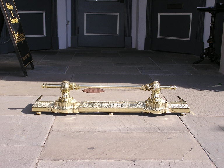 French brass fire place fender with centered upper bar supported by flanking intertwined dolphins, hand chased acanthus motif, and terminating on ball feet.  Mid 19th Century