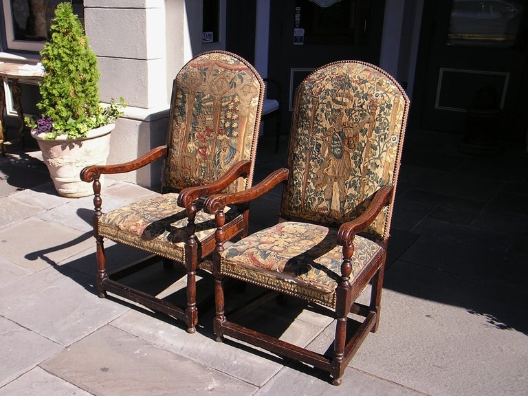 Pair of Italian walnut armchairs with arched top, floral carved scrolled arms,  original needlepoint, and terminating on bulbous turned legs with stretchers. 18th Century 