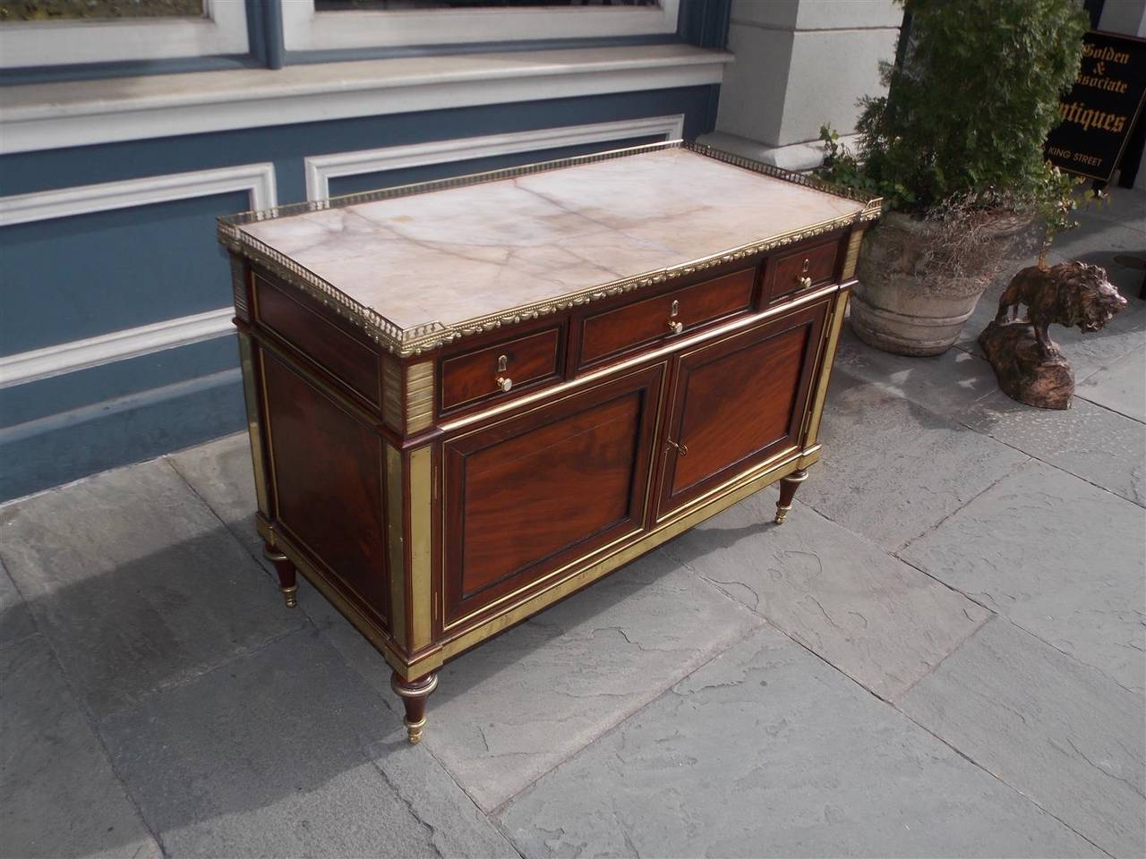 French mahogany three-drawer marble-top commode with pierced brass beaded and tassel gallery, inlaid brass mounts, lower two-door cabinet and terminating on bulbous tapered ormolu feet . Late 18th century. All original with engraved brass dated