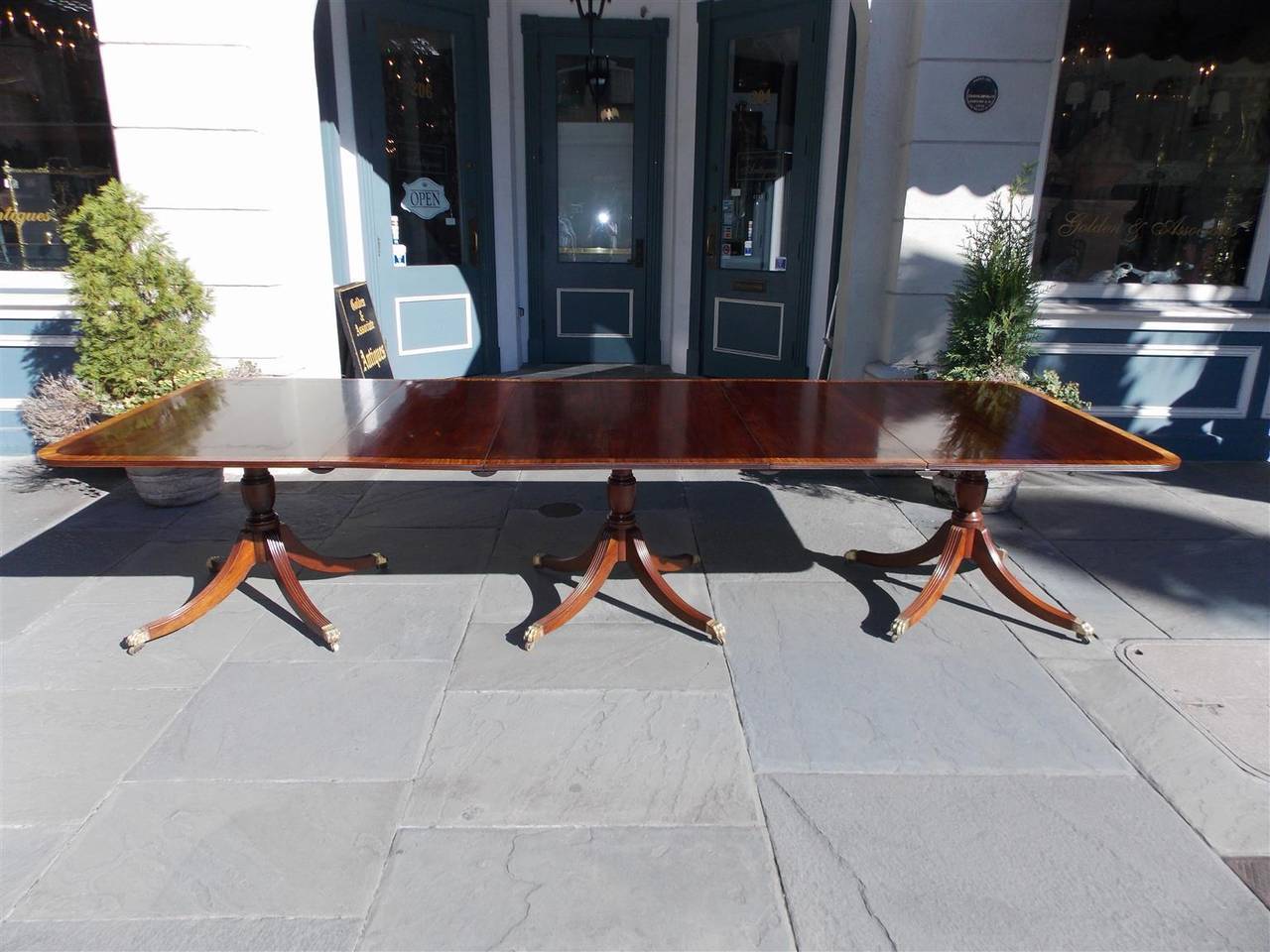 English mahogany triple pedestal tilt-top dining room table with cross banded satinwood, original two removable leaves, terminating on saber legs with original lions paw brass casters, Early 19th century. Table can be used without two leaves and