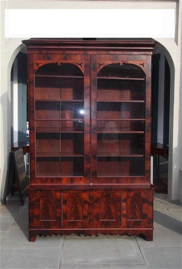 American book matched crotch mahogany two door glass front bookcase with gadrooned molded edges,  adjustable interior shelving, lower fitted compartmentalized cabinets over intricate carved skirt, and terminating on bracket feet. Mid 19th Century