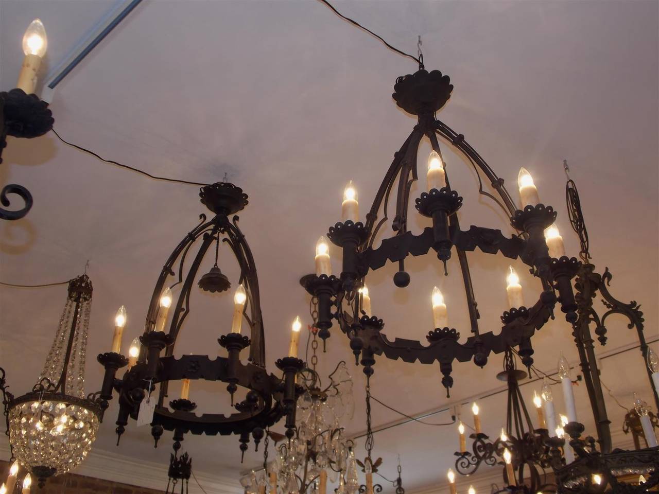 Pair of American wrought iron eight-light circular chandeliers with decorative cut work, pierced bobeches, floral medallions, ball finials, and original canopies. Originally gas powered and have been electrified, Mid-19th century.