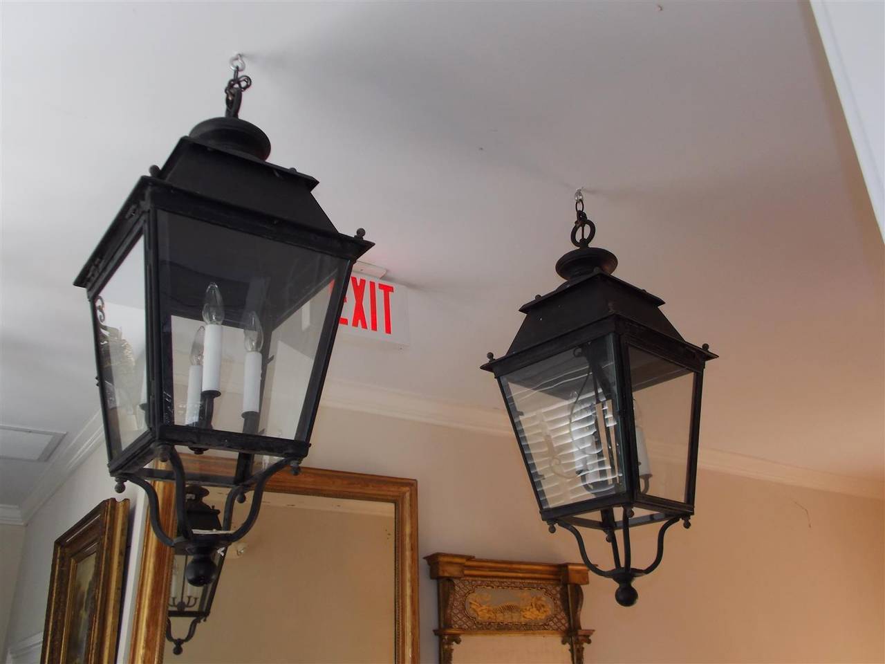 Pair of French wrought iron hanging lanterns with graduated squared tops , glass hinged doors, and terminating on the original decorative scrolled brackets with ball finials. Originally gas powered and have been electrified, Second half of the 19th