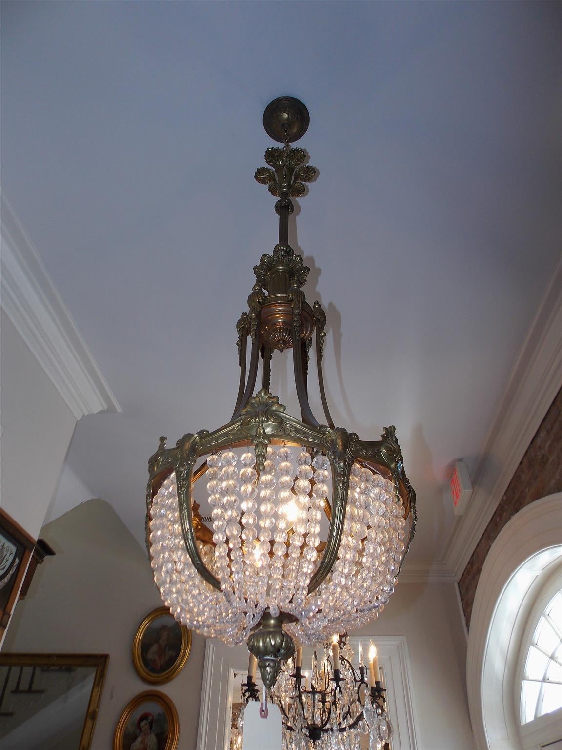 Araña francesa de bronce dorado y cristal de cuatro luces con dosel decorativo floral, una columna acanalada centrada que sostiene una cesta inferior de cristal iluminado de seis brazos, completada con un motivo decorativo de flor de campana y