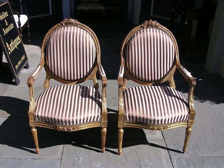 Paire de fauteuils à dossier ovale en bois sculpté et doré, à motif floral entrelacé et articulé, se terminant par des médaillons d'angle floraux et des pieds cannelés en forme de bulbe. Les chaises ont été recouvertes d'une soie rayée.  Milieu du