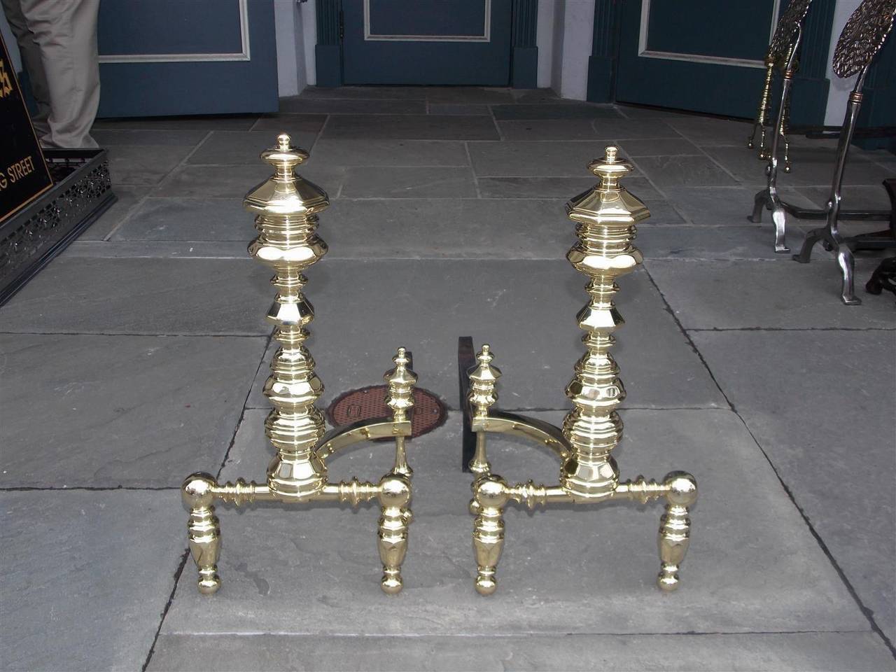 Pair of American brass andirons with faceted finials, faceted centered plinths, and terminating on turned bulbous feet with matching log stops. Signed E. Smylie New York, Early 19th century.