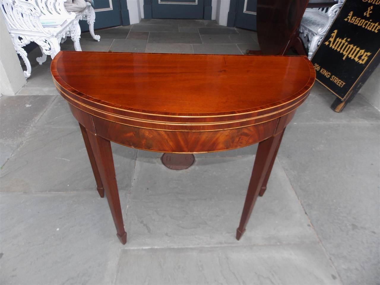 English Hepplewhite crotch mahogany flip top game table with Satinwood string inlay, Tulip wood cross banding, baise lined interior and terminating on tapered squared legs with spade feet. Late 18th Century