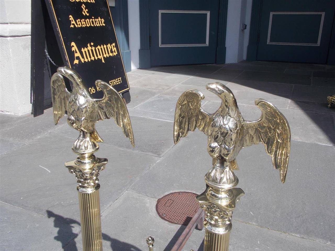 Pair of American brass andirons with perched eagles on top of ball finials, reeded Corinthian column plinths and terminating on scrolled foliage legs with ball feet and original finial log stops. Signed New York, Late 19th century.