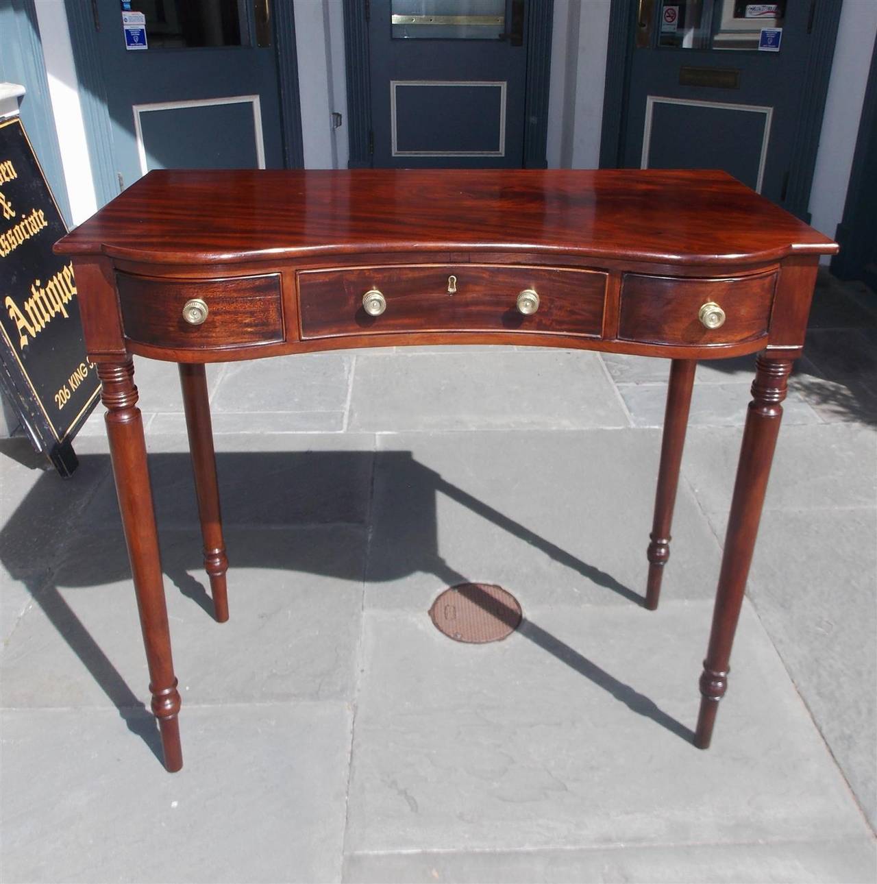 Jamaican mahogany serpentine three drawer server with a one board surface, original brasses, and terminating on the original turned bulbous ringed legs.  Early 19th Century.