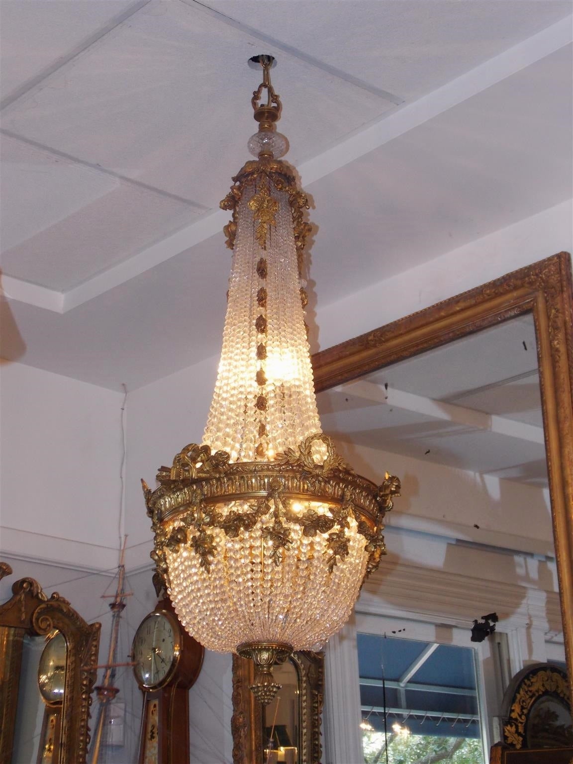 French gilt bronze and crystal eight light basket chandelier with decorative gilt floral swags, laurel wreath, graduated cascading bell flowers, and terminating with an artichoke finial.  Early 19th Century.  Originally candle powered and has been