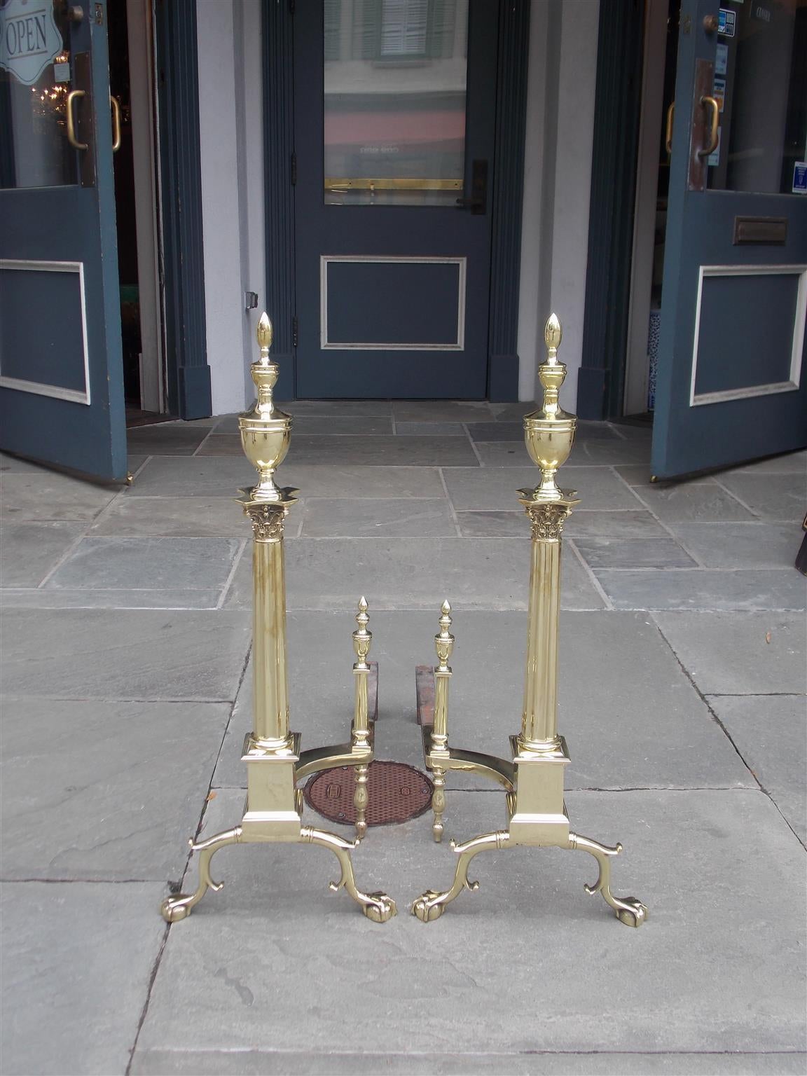 Pair of American brass andirons with urn top finials, Corinthian fluted columns, squared plinths, double spurred legs and terminating on ball and claw feet. Philadelphia, Circa 1870.