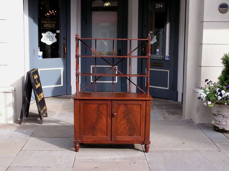 English Regency book matched mahogany bookcase with three tiered shelving, cross hatching, turned bulbous ringed columns with urn finials, wooden knob, fitted interior shelving, and resting on the original cone bracket feet. Early 19th Century