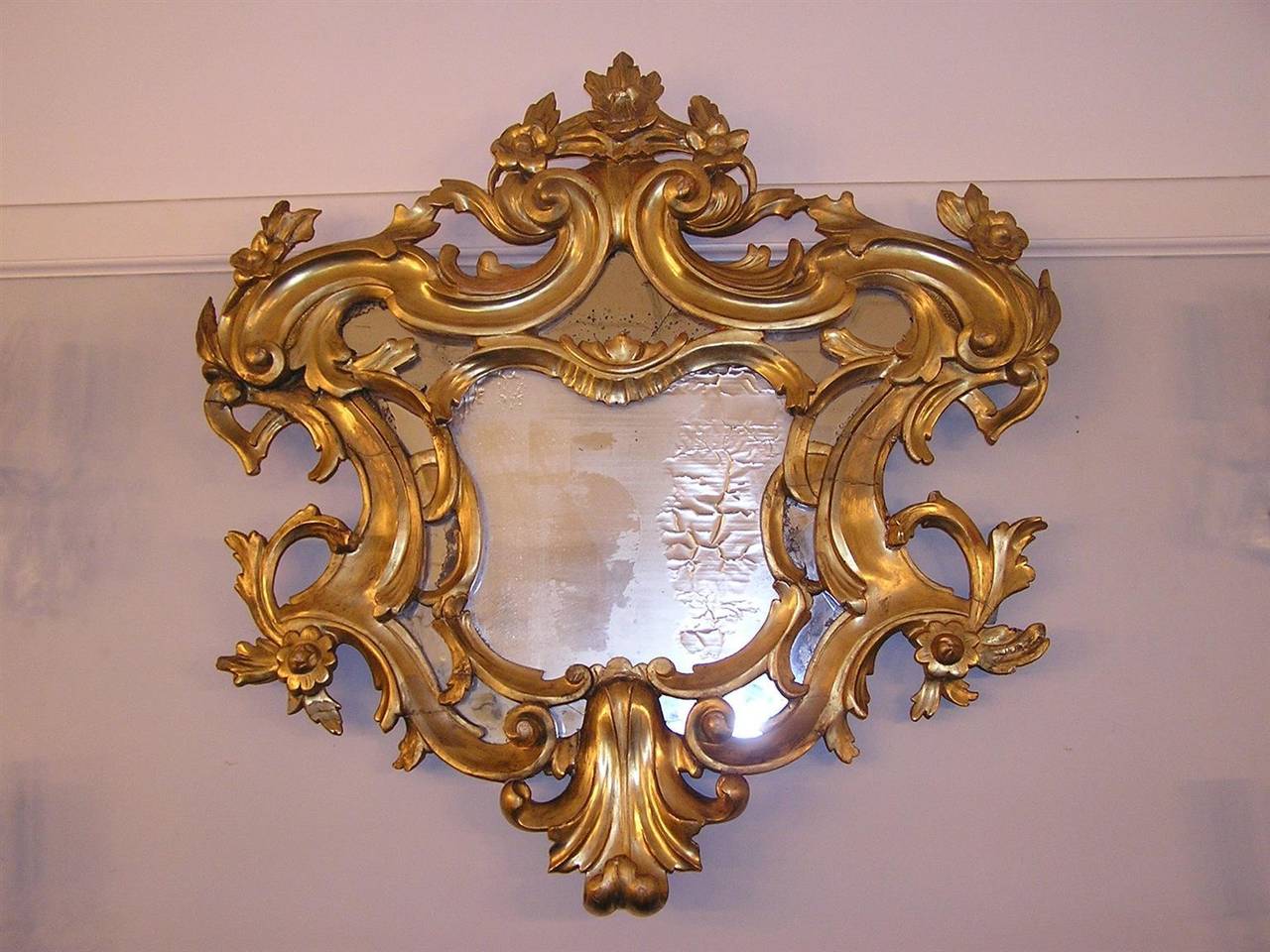 English carved wood gilt decorative floral wall mirror with original glass and wood back. Late 18th century.