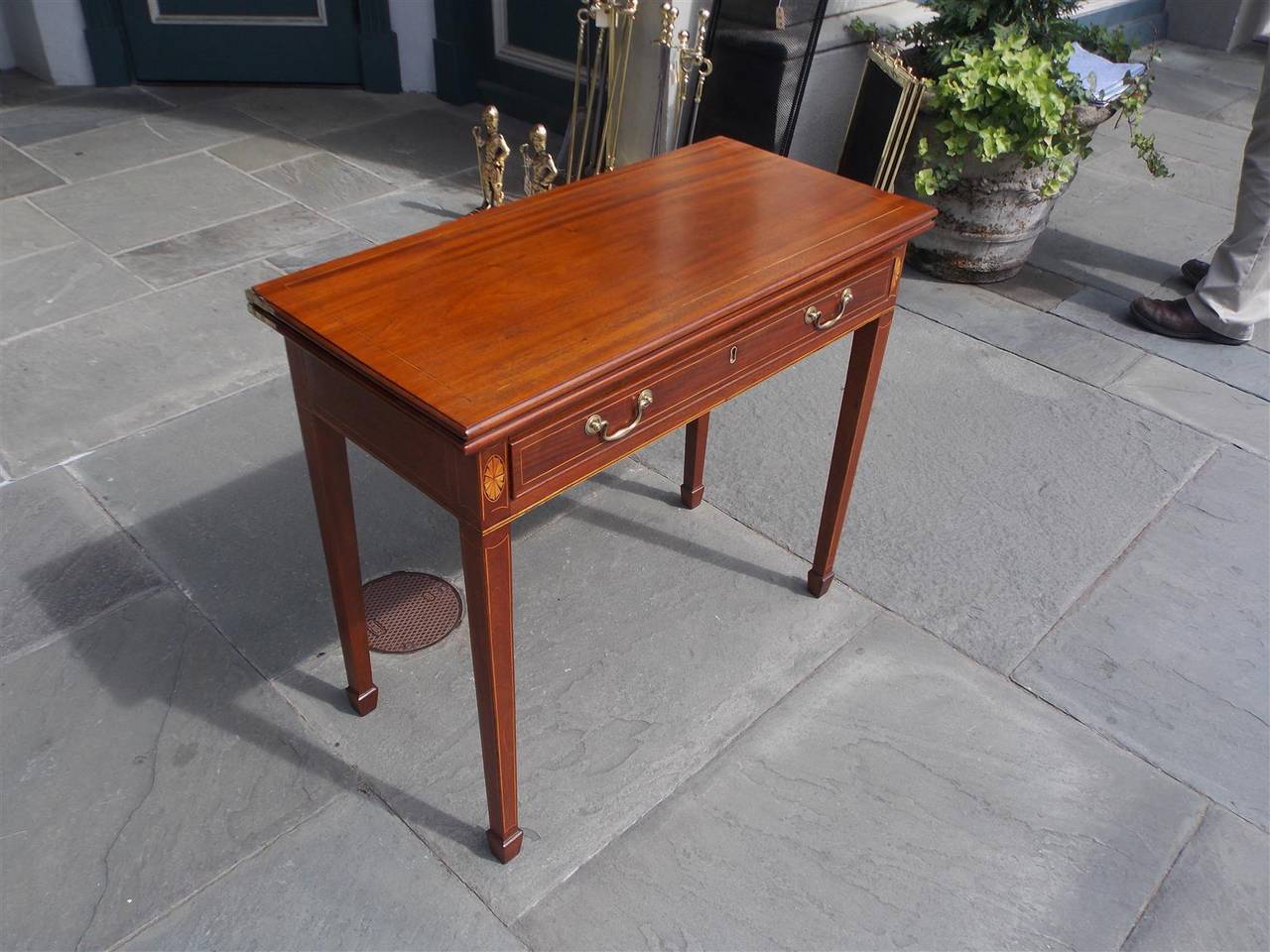 American mahogany one board hinged top single-drawer card table with original brass pulls, satinwood string inlay, corner patera's, and terminating on squared tapered legs with spade feet. Table has gate leg to support top when open, Early 19th