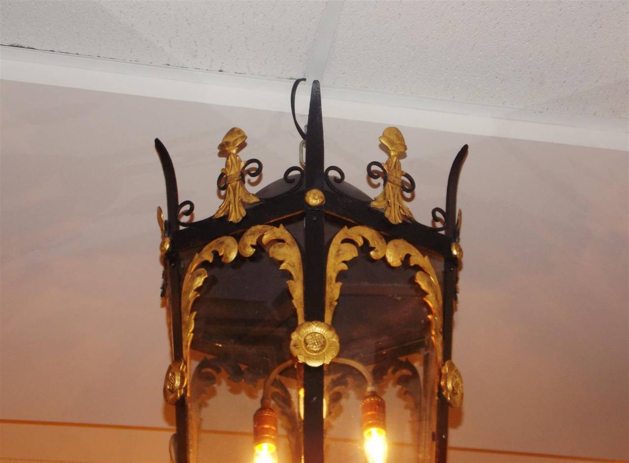 American wrought iron and gilt three-light hanging lantern with six-paneled glass sides, decorative gilt acanthus and floral medallions, adorned with upper and lower scrolled spikes with decorative domes. Originally gas and has been electrified.