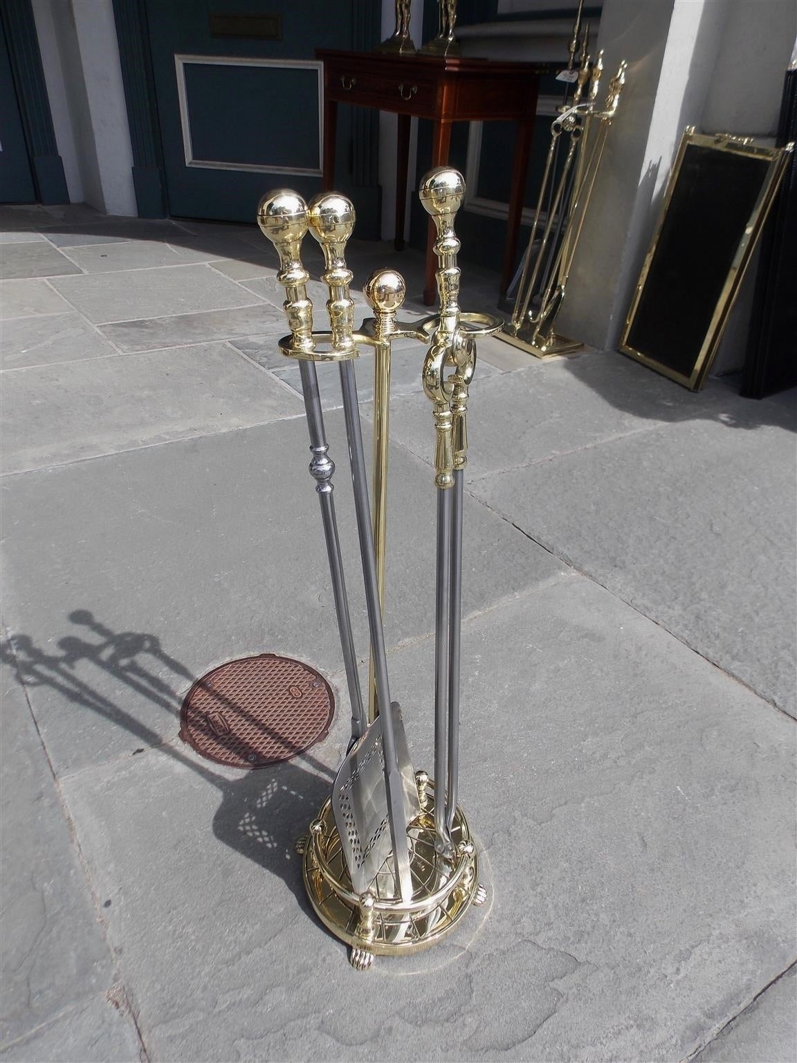 Set of American brass ball top and polished steel fire tools resting on decorative circular stand with gallery and lions paw feet. Set consist of shovel, tong, and poker. Boston, Mid 19th Century