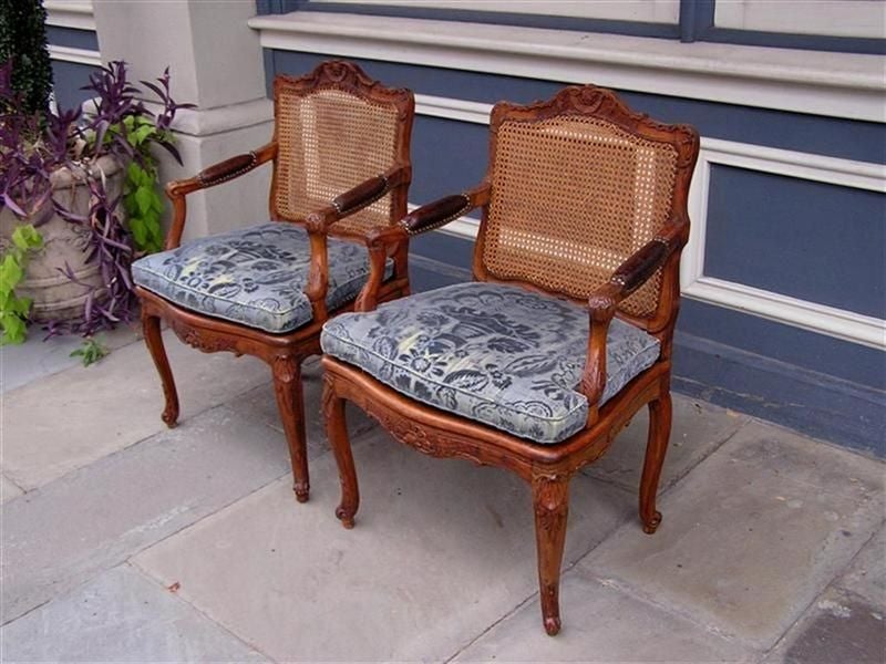 Pair of French Walnut foliage and shell arm chairs with original cane backs and seats, leather arms, upholstered seats, and resting on scrolled cabriole legs. Early 19th Century