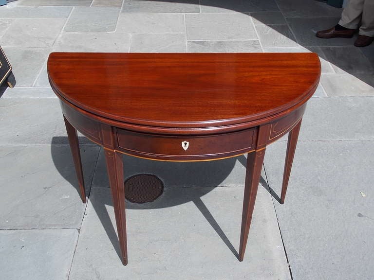 English mahogany one drawer flip top demi-lune game table with one board top, Satinwood string inlay, original key escutcheon, and terminating on double gate tapered squared legs.  Late 18th Century