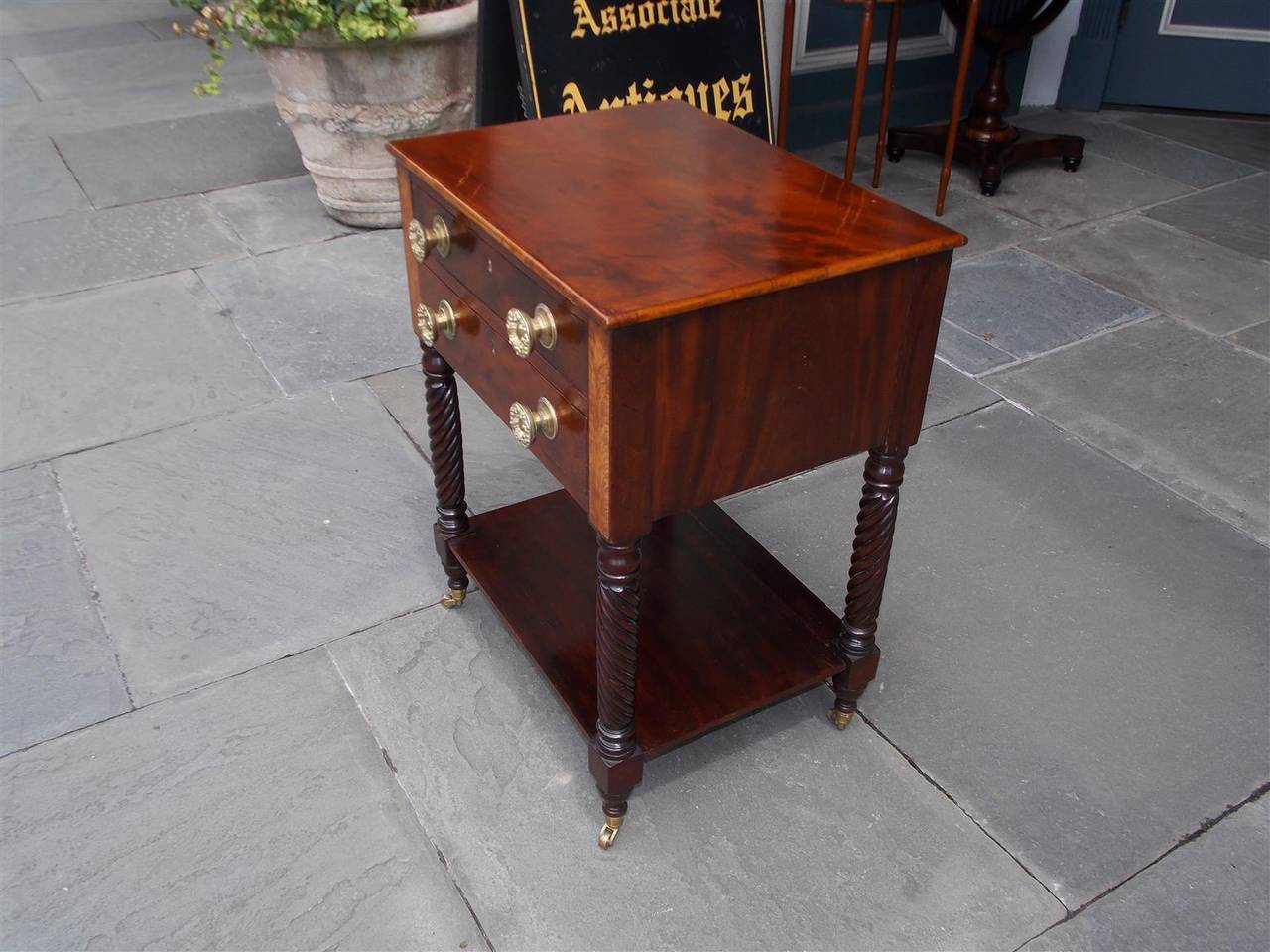 American mahogany two-drawer side table with inlaid flanking satinwood panels, original floral brasses, lower shelf, and terminating on barley twist legs with original brass casters. Table is finished on all sides. Early 19th century.