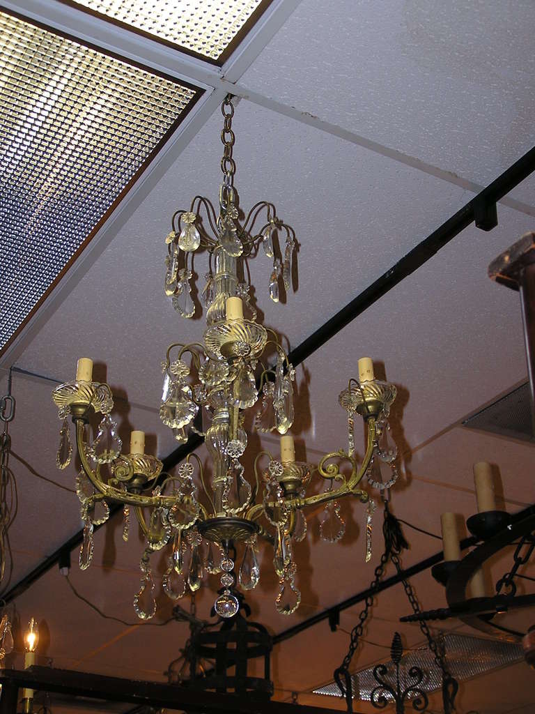 Französischer Kronleuchter aus vergoldeter Bronze und Kristall mit fünf Lichtern, mittig angeordneter bauchiger Kristallsäule und dekorativem, verschlungenem Blumenmotiv.  Ursprünglich mit Kerzen betrieben, wurde es elektrifiziert. Anfang des 19.