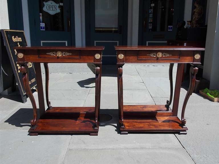 Pair of English Regency mahogany one drawer consoles with ormolu mounts, scrolled legs, original mirrors, and terminating on block feet.  Late 18th Century