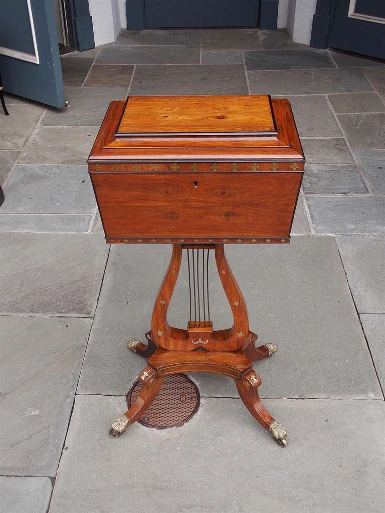 English Regency mahogany rectangular hinged tea poy with fitted interior bins, central lyre pedestal, foliage brass inlays, flanking gilt floral pulls, and resting on saber legs with the original brass claw casters. Early 19th Century  