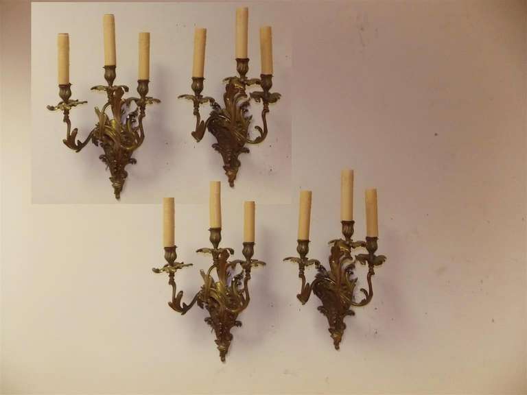 Set of four French gilt bronze scrolled three-arm sconces with floral motif. Originally candle powered and have been electrified. Early 19th Century.