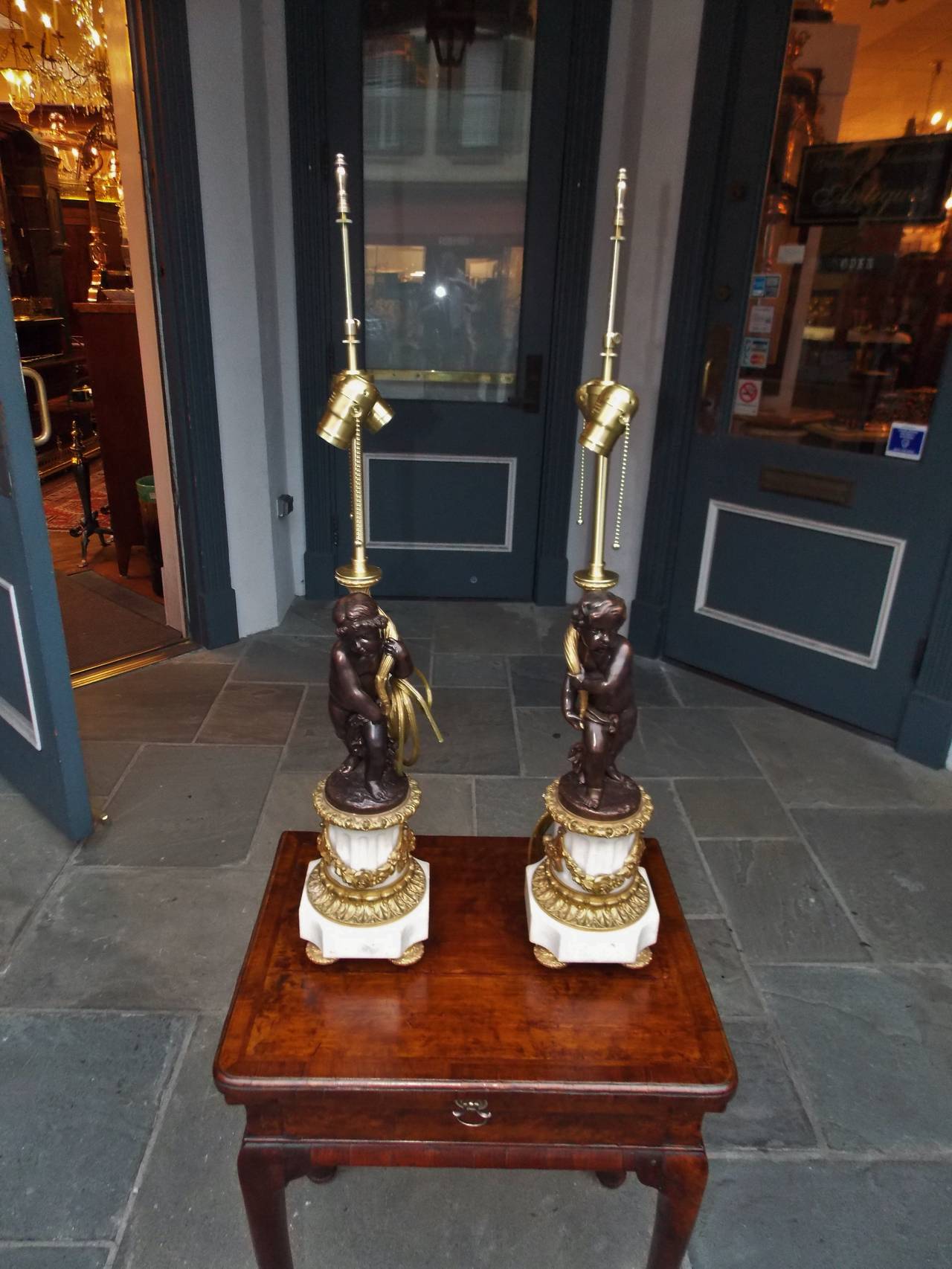 Pair of French ormolu bronze and fluted marble cherub table lamps with decorative floral swags, lambs tongue, and resting on decorative gilt bronze circular feet. Originally candle powered and has been electrified,  Early 19th Century.