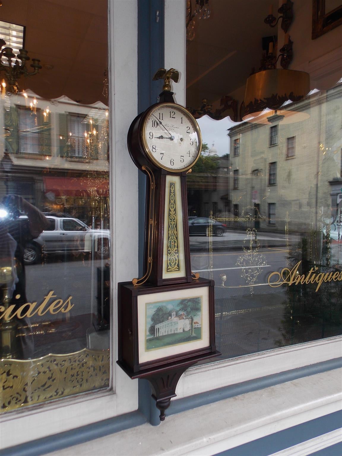 American mahogany banjo clock with a perched eagle finial, steel engraved dial under glass, centered decorative gilt reversed painted glass, lower hinged door with a reverse painting of Mount Vernon, flanking brass galleries, and terminating with a