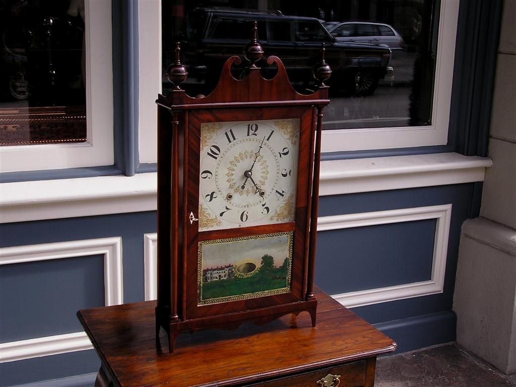 American mahogany pillar and scroll clock  with original carved scroll pediment, finials, works, reverse painted glass, and feet. Clock has original paper label( Made and sold by Olcott Cheney Middletown Connecticut) and is in working condition.