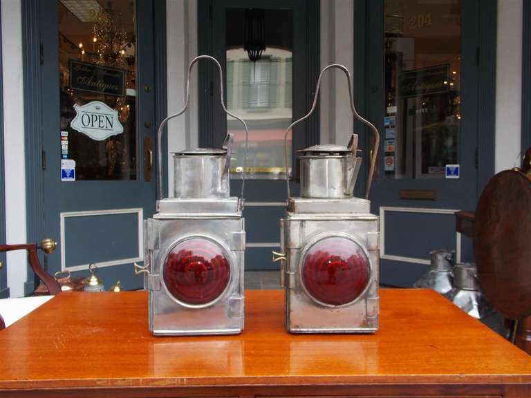 Pair of American polished steel railroad Signal lanterns with flanking hinged doors, scrolled carrying handles, vented tops, rear mounting brackets, and the original Fresnel circular red lenses. Originally oil and can be electrified if desired. Late