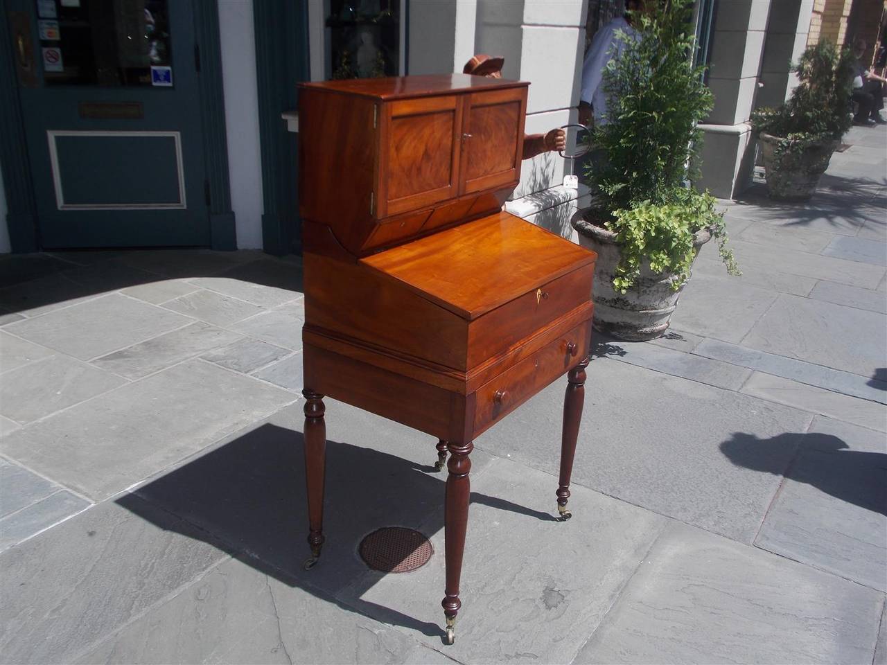American Sheraton mahogany Campaign slant front desk with two upper case flanking doors concealing pigeon holes, sliding lower case writing surface concealing fitted interior over single drawer and terminating on turned bulbous legs with original