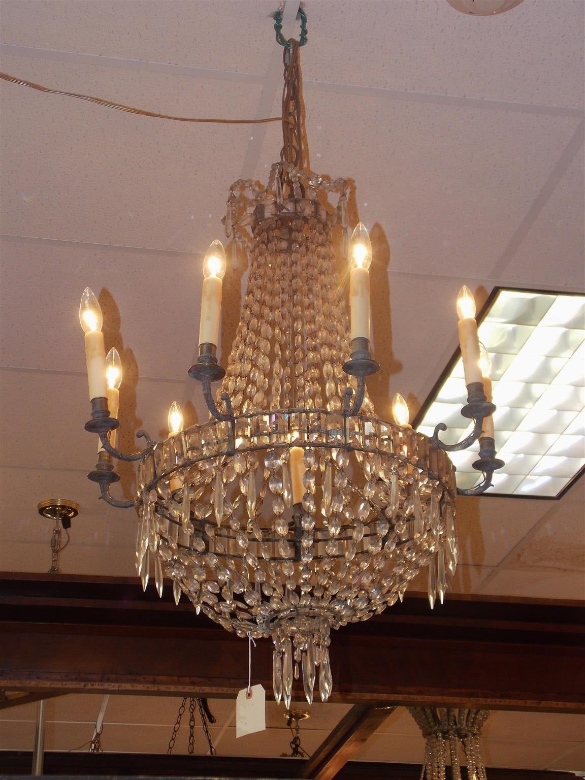 English Regency bronze and crystal nine-light chandelier with beaded and squared crystal canopy, cascading crystal strands, bronze floral motif scrolled arms, and terminating with a lower decorative crystal basket, Early 19th century. Chandelier was
