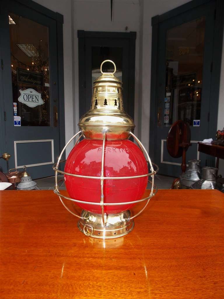 American brass ship boarding onion lamp with protective brass cage surrounding Red Perkins globe, vented top, and original removable tank with burner. New York  Early 20th Century