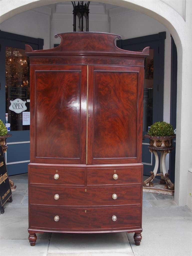 English Regency mahogany bow front linen press with scrolled pediment, fitted interior, pull out upper shelving, four drawer lower case, and ending on turned bulbous feet.  Dealers please call for trade price.   