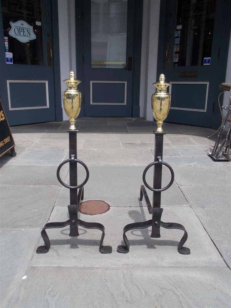 Pair of American brass urn finial and wrought iron andirons with flanking central rings, spit hooks, and resting on scrolled legs with stylized penny feet. Early 19th Century.