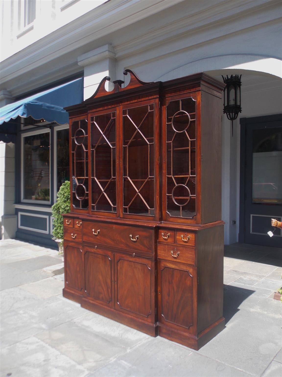 English Chippendale mahogany broken pediment breakfront with carved floral medallions, candle light molding, four upper case glass doors with adjustable shelving, lower case concealing a sliding fall front desk, flanking drawers with original