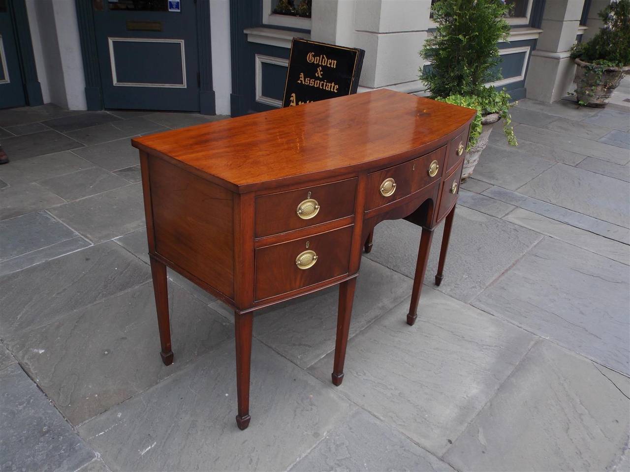 English Hepplewhite mahogany five-drawer bow front sideboard with carved scalloped skirt, original brasses, and terminating on tapered legs with spade feet. Sideboard has a one board top, Early 19th century.