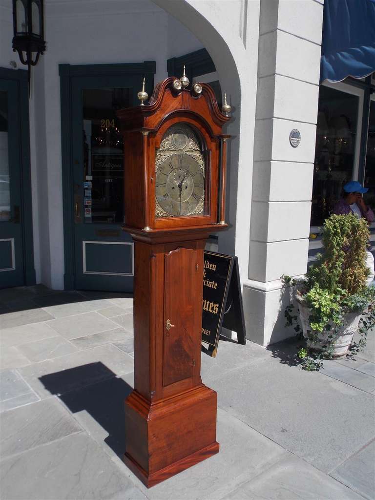 American walnut Chippendale tall case clock with broken arch pediment bonnet, brass finials, brass mounted columns, gilded face with dolphin motif, and terminating on squared plinth .  Clock is in working condition. 18th Century