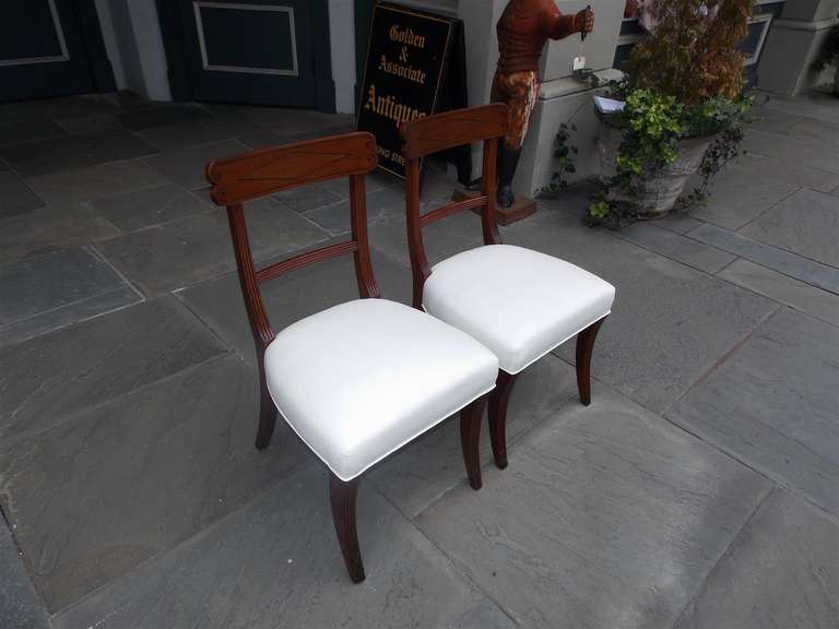 Pair of English Regency side chairs with ebony string inlay, upholstered seat, and terminating on reeded saber legs with carved foliage feet. Early 19th Century.  Chairs are covered in white muslin.