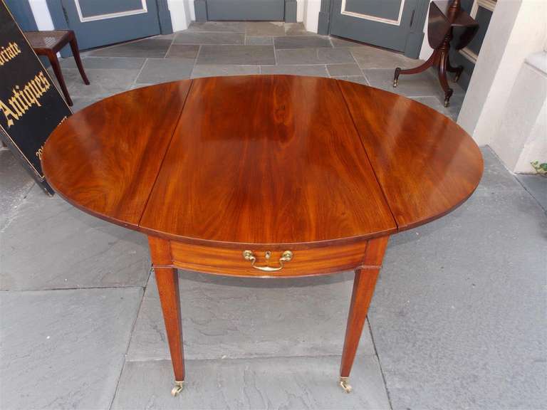 English mahogany drop leaf pembroke table with one board top, single drawer, original brasses, and terminating on tapered legs with original brass casters. Late 18th Century.  Table is 51