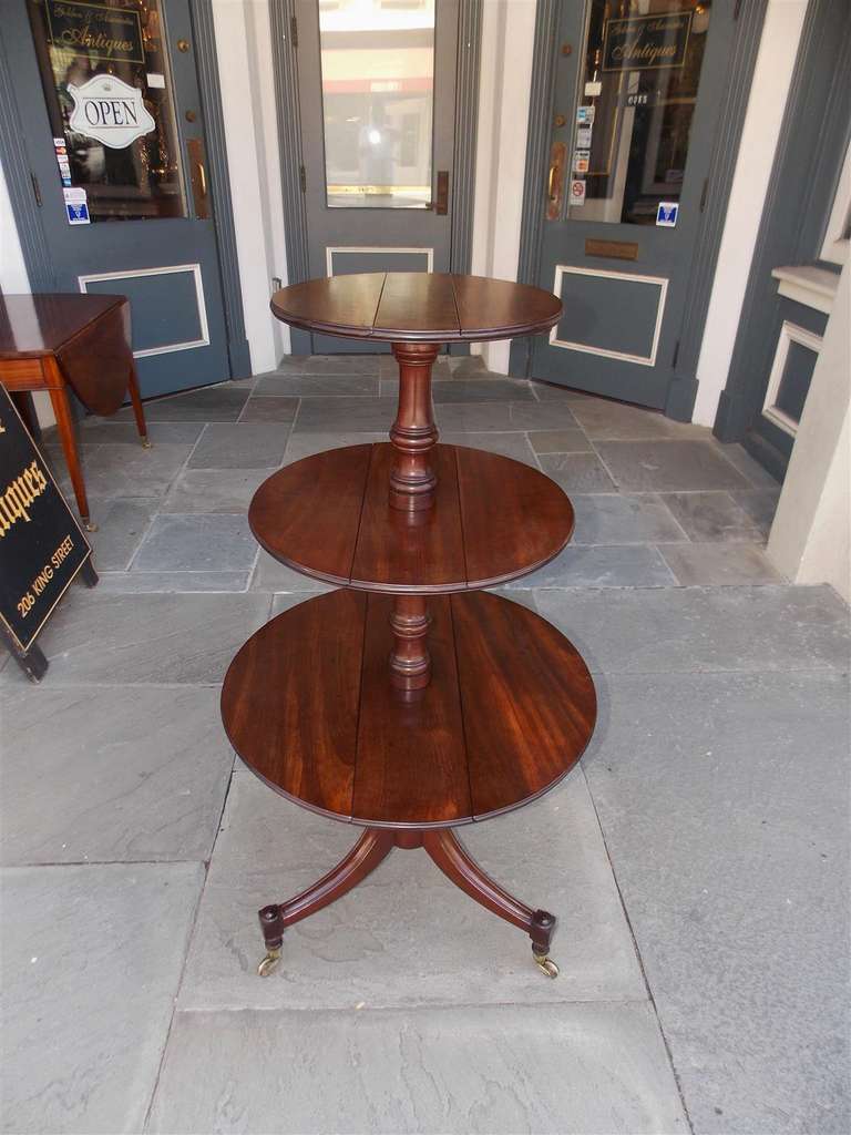 English mahogany three tier dumb waiter with hinged tops, bulbous turned center column, and terminating on reeded splayed legs with original brass casters. Late 18th Century