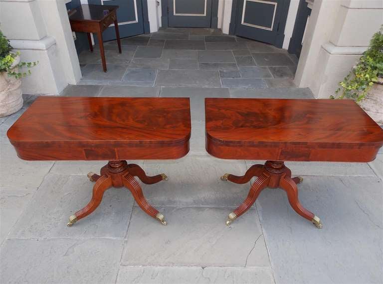 Pair of American mahogany flip top card tables with baize interior top, turned bulbous floral pedestal, and terminating on reeded saber legs with original brass casters.  Philadelphia, Early 19th Century