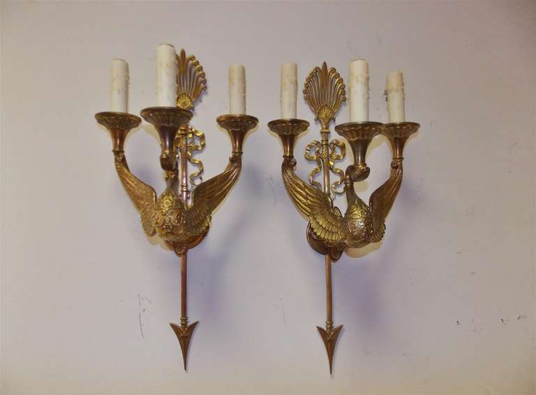 Coppia di appliques francesi a tre bracci in bronzo dorato con motivi di cigni, nastri, filigrana e frecce. Originariamente alimentato a candela. Inizio del XIX secolo.