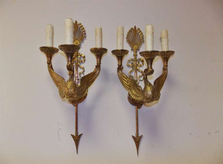 Pair of French gilt bronze three arm sconces adorned with swans, ribbon, filigree, and arrow motif. Originally candle powered. Early 19th century.